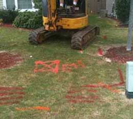 Broken sewer line below a maze of power and cable lines - red and orange paint indicate the location of the buried utilities